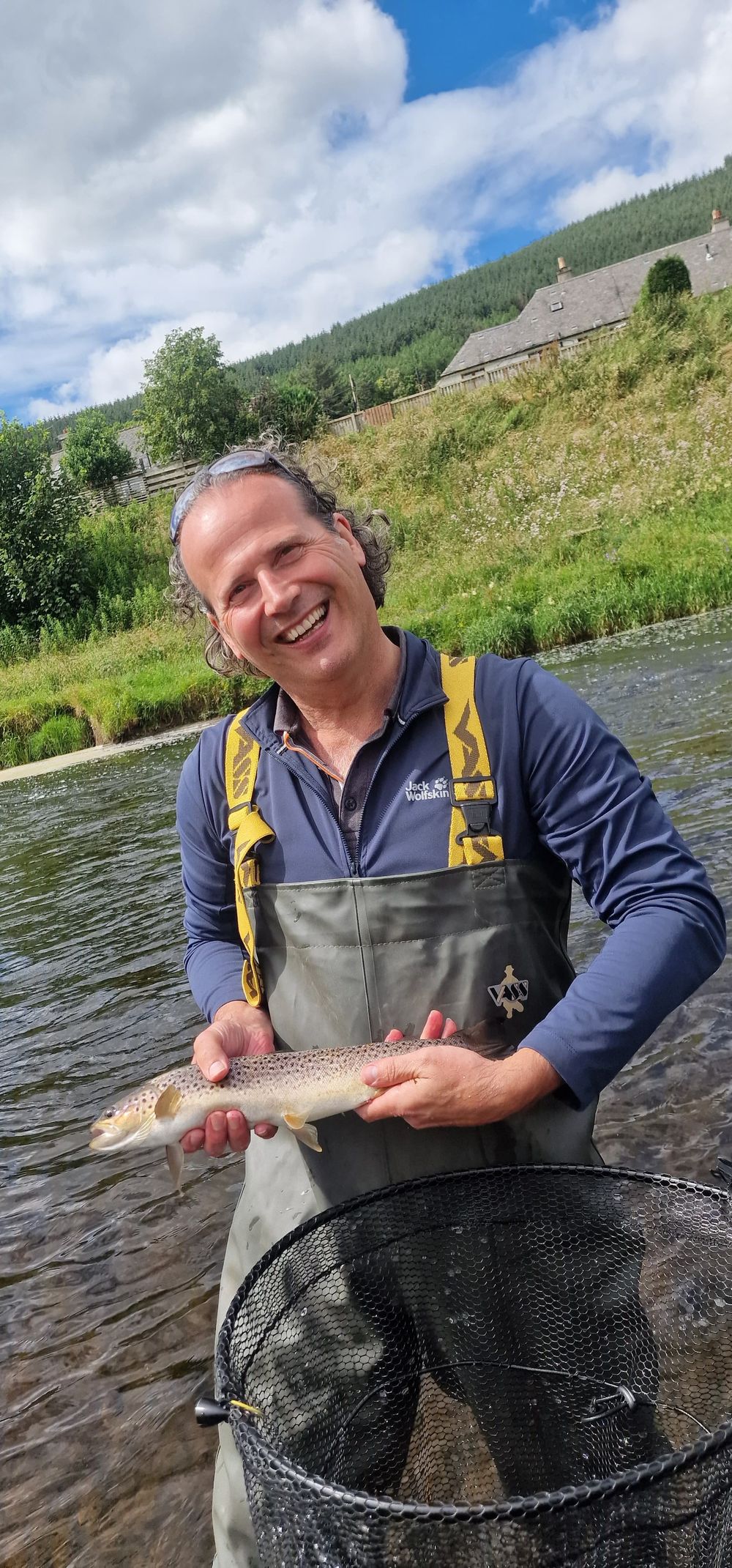 Happy client holding a wild brown trout on a sunny summer day