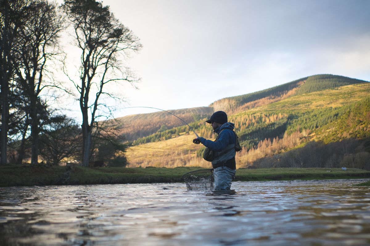 Fly fishing at golden hour on a Scottish river with hills behind